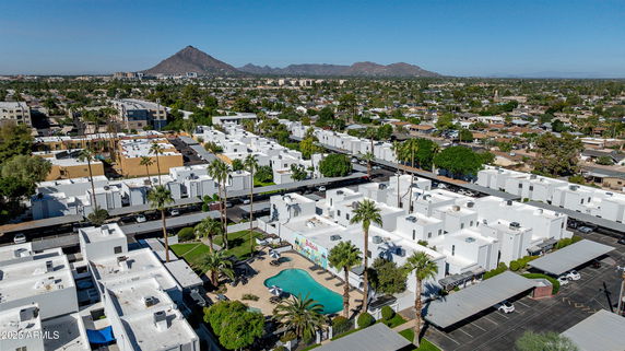 Aerial panoramic view of white residential buildings with a central swimming pool and mountainous background.