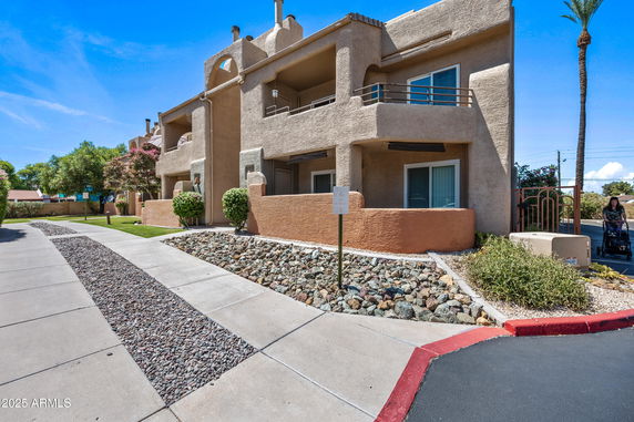 Front view of a multi-story building with balconies and a stone-lined path.