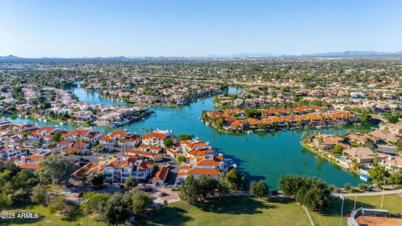 Wide aerial view of a residential area with houses surrounded by waterways and greenery.