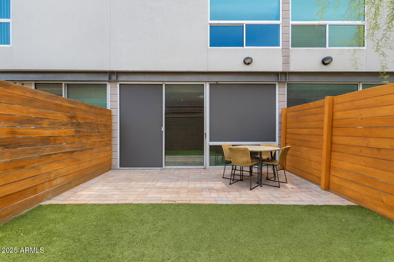 Front view of a modern building with a small outdoor patio area, wooden fencing, and glass doors.