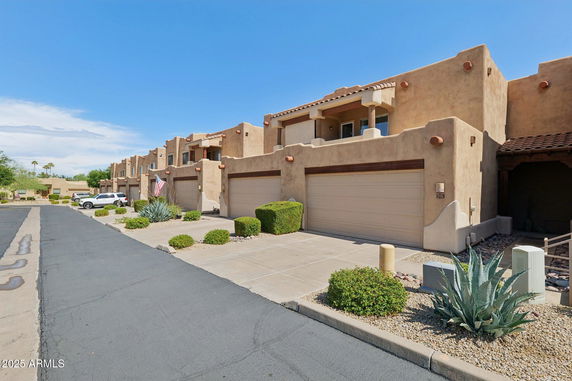 Front view of a row of two-story adobe-style townhouses with garages.
