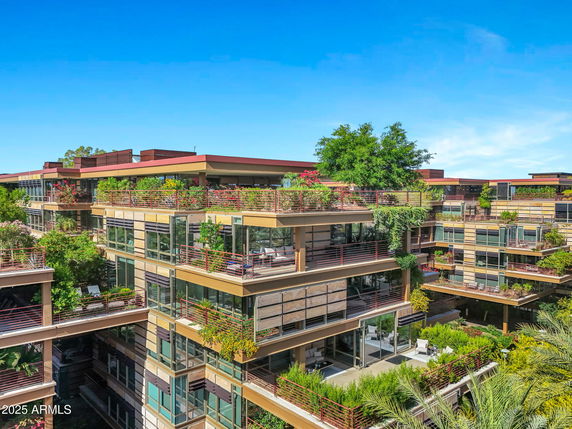 Front view of a multi-story modern apartment building with extensive greenery on balconies.