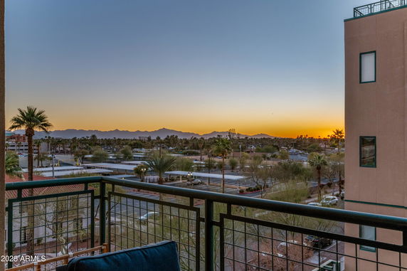 Panoramic view from a building balcony overlooking a sunset and distant mountains.