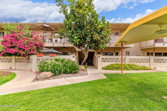 Front view of a two-story residential building with balconies and surrounding plants.
