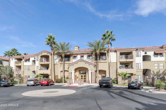 Front view of a three-story residential building with balconies and a landscaped entrance.