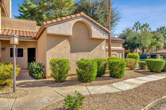 Front view of a single-story building with a tiled roof and surrounding shrubs.