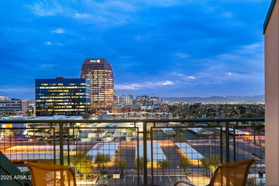 Panoramic view of a cityscape from a building, showcasing multiple illuminated buildings and a clear evening sky.