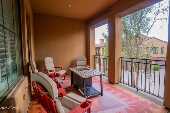 Balcony with chairs and a table, overlooking adjacent building and trees.