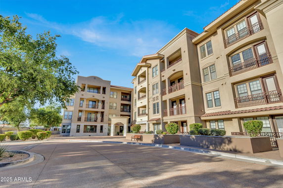 Front view of a multi-story apartment building with balconies and a paved entrance.