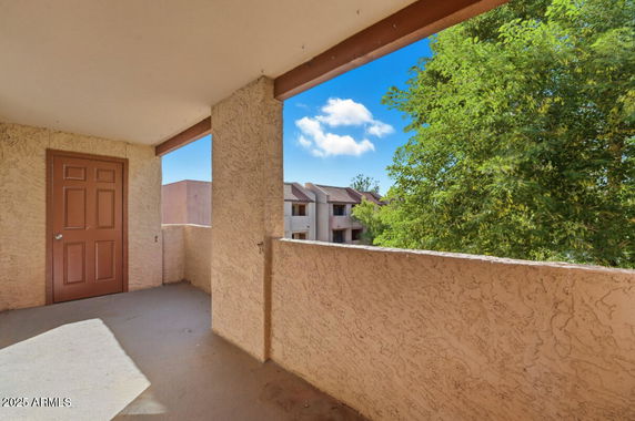 Outdoor balcony view with nearby buildings and trees.