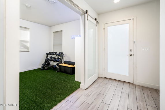 Indoor space with exercise equipment and green flooring adjacent to a bright entryway.