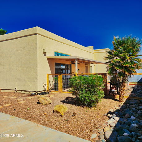 Front view of a small, modern, single-story building with a fence and a patio area.