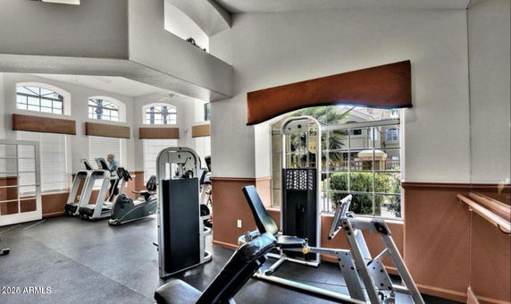 Interior view of a gym with various exercise equipment and bright windows.