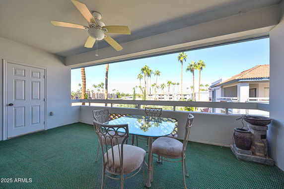Outdoor seating area with a ceiling fan and a view of palm trees and surrounding buildings.