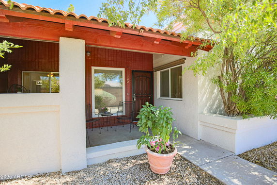 Front view of a house with a small porch, red wooden accents, and a potted plant.