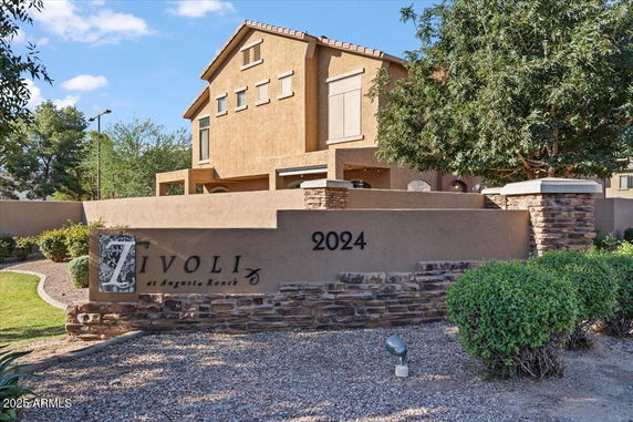 Front view of a two-story house with a beige stucco exterior and a sign reading 'Tivoli at Augusta Ranch.'