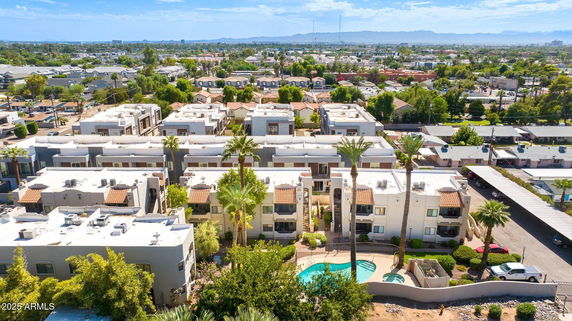 Panoramic view of a residential complex with multiple buildings and a swimming pool, surrounded by greenery and urban landscape.