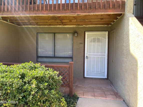 Front view of a house entrance with a white door and wooden railing above.