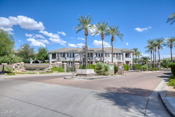 Front view of a multi-story residential building with palm trees and gated entrance.