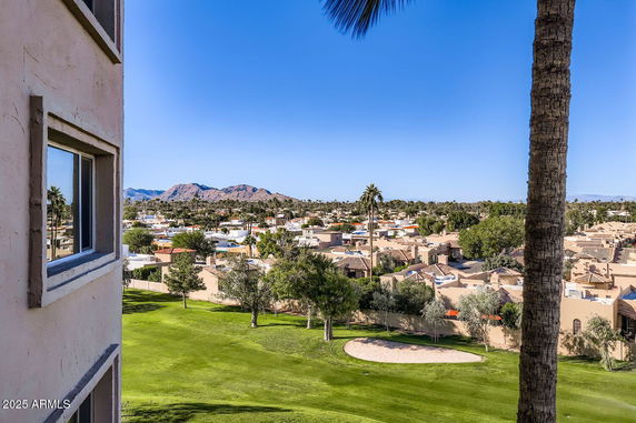 Panoramic view from a building showing a landscape with houses, green fields, and distant mountains.