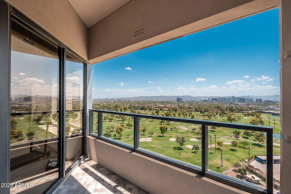 Panoramic view from a building balcony overlooking a vast landscape with a golf course and distant city skyline.