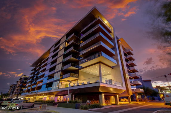 Front view of a modern multi-story building with balconies at dusk.