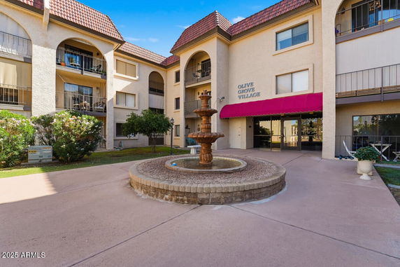 Front view of a multi-story building with balconies and an entrance, featuring a central fountain.