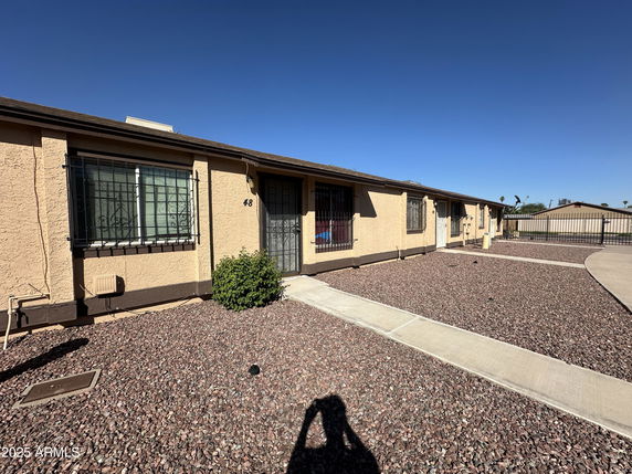 Front view of a single-story house with barred windows and a gravel landscape.