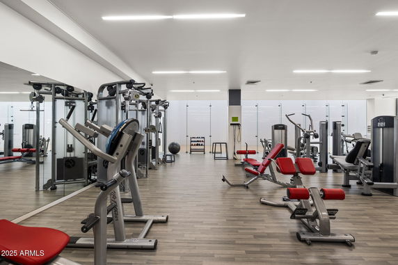 Interior view of a gym with various exercise equipment, mirrors, and wooden flooring.