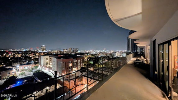 Panoramic view of a cityscape at night from a building's balcony, showing a wide expanse of buildings and city lights.