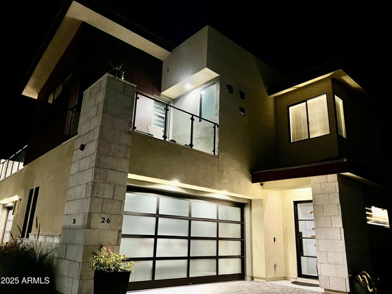 Front view of a modern two-story house at night with a glass garage door and illuminated windows.