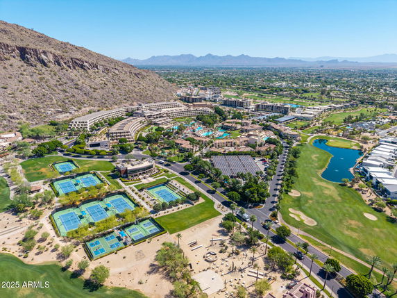 Panoramic aerial view of a resort area with tennis courts, swimming pool, and surrounding landscape.