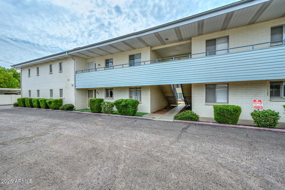 Front view of a two-story apartment building with a covered walkway and green shrubs.