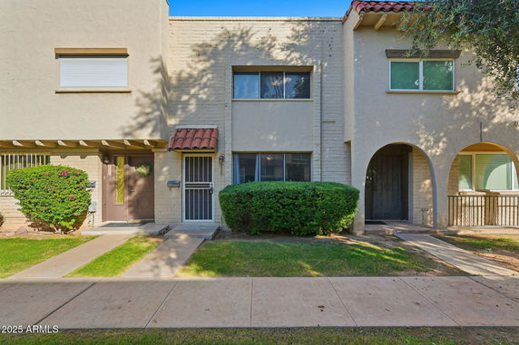 Front view of a small two-story townhouse with a simple facade and small entrance walkway.