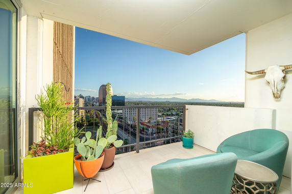 Balcony view from a high-rise building with urban skyline and mountains in the background.