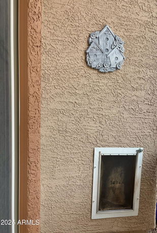 Close-up view of a textured exterior wall with a pet door and decorative wall ornament.