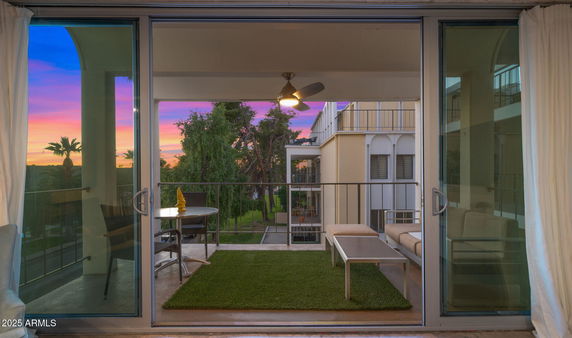View from a balcony with seating area overlooking surrounding trees and building during sunset.