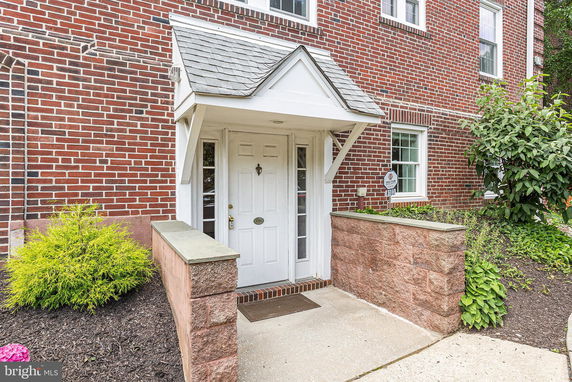 Front view of a brick building entrance with a white door and small overhang.