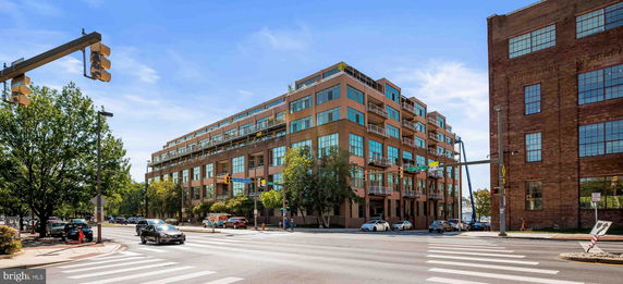 Front view of a multi-story modern building with balconies and large windows situated on a street corner.