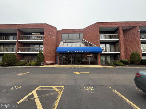 Front view of a multi-story condominium building with balconies and a glass entrance canopy.