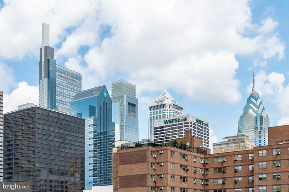 View of multiple skyscrapers in a city skyline with various architectural designs and a brick apartment building in the foreground.
