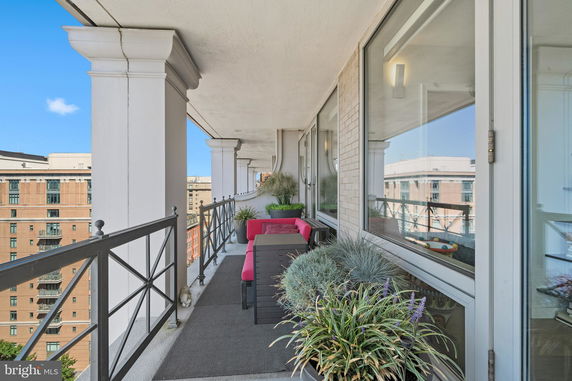 Balcony view with seating and potted plants overlooking surrounding buildings.