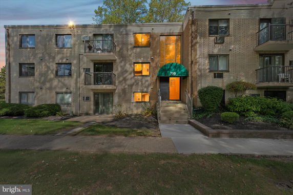 Front view of a three-story brick apartment building with balconies and an entrance canopy.
