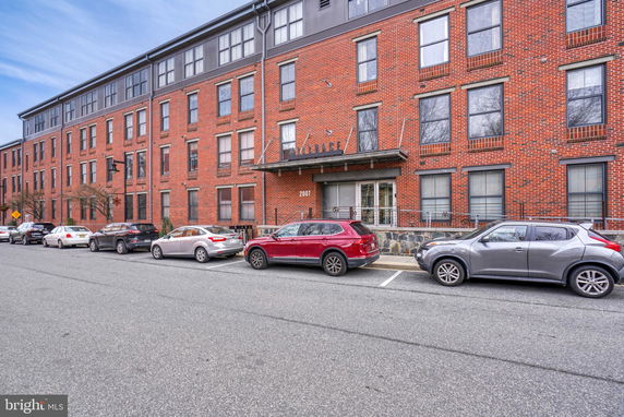 Front view of a multi-story brick building with large windows and a street parking area.