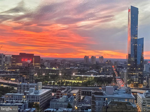 Panoramic view of city skyline during sunset with a prominent tall building and vibrant sky.