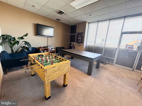 Room with a foosball table, seating area, and a television on the wall.
