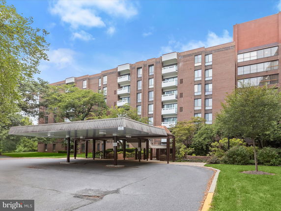 Front view of a multi-story brick residential building with balconies and a covered entrance area.