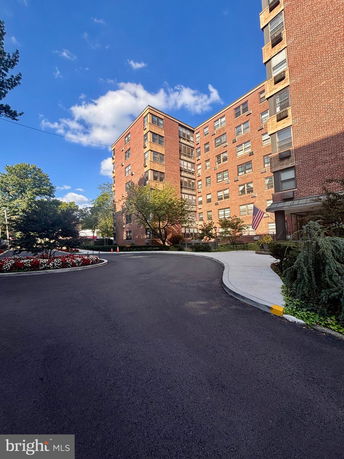 Front view of a multi-story brick apartment building with a curving driveway.
