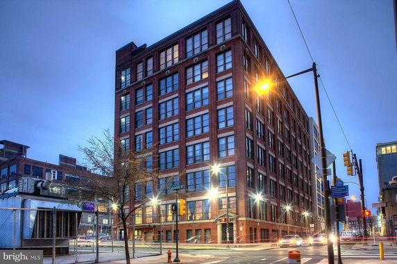 Front view of a multi-story brick building at a street corner with illuminated streetlights.