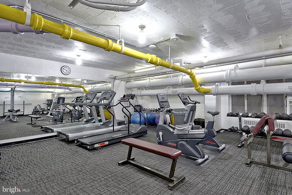 Indoor gym area with exercise equipment and yellow pipes on the ceiling.